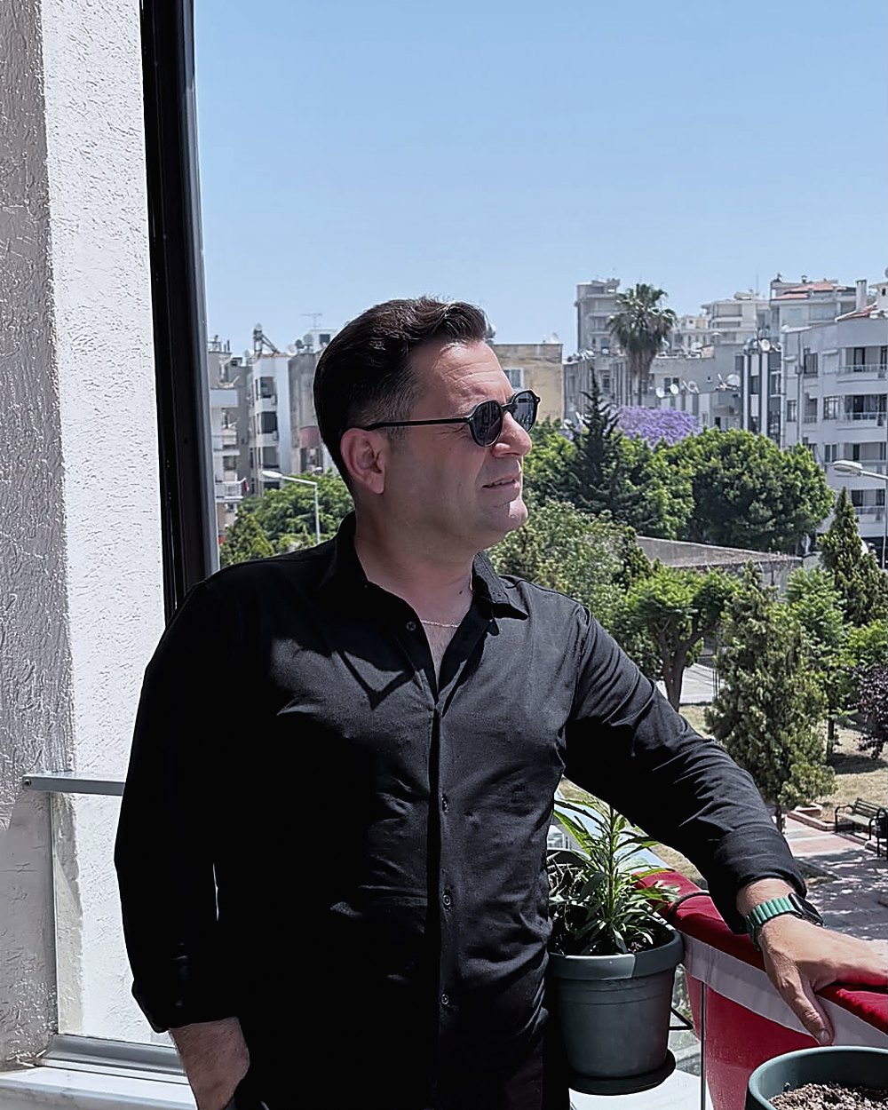 Feridun Özpolat, siyah gömlek ve güneş gözlüğüyle balkonda dururken