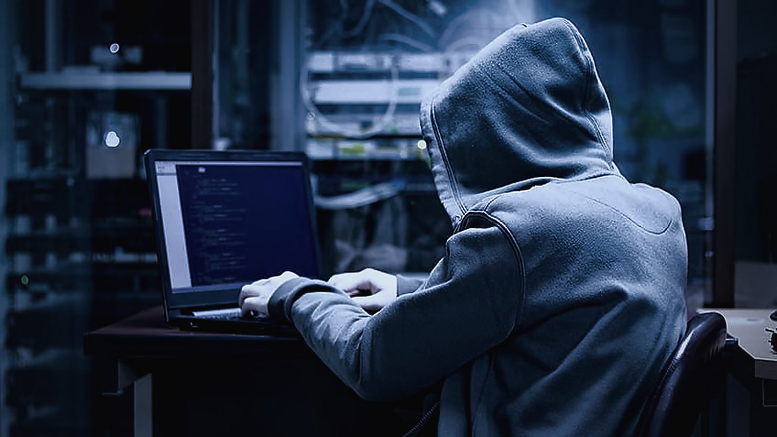Sunucu odasında açık gri kapüşonlu bir kişi dizüstü bilgisayarda çalışıyor — white hacker temalı temsili görsel